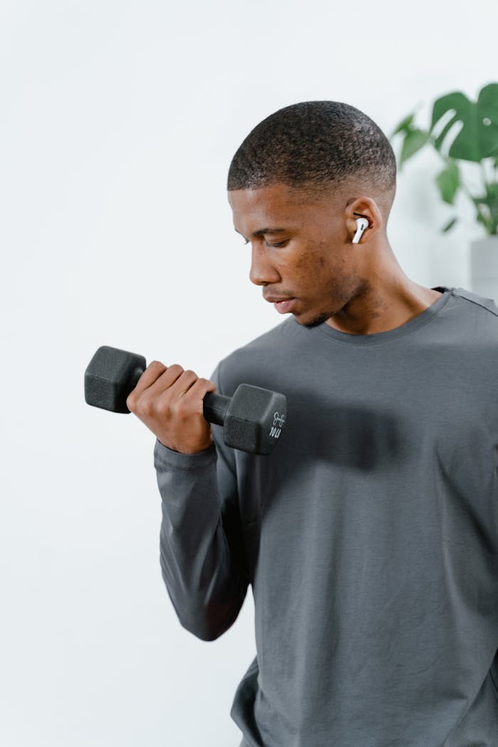 A young man in activewear lifting a dumbbell indoors, focused on fitness.