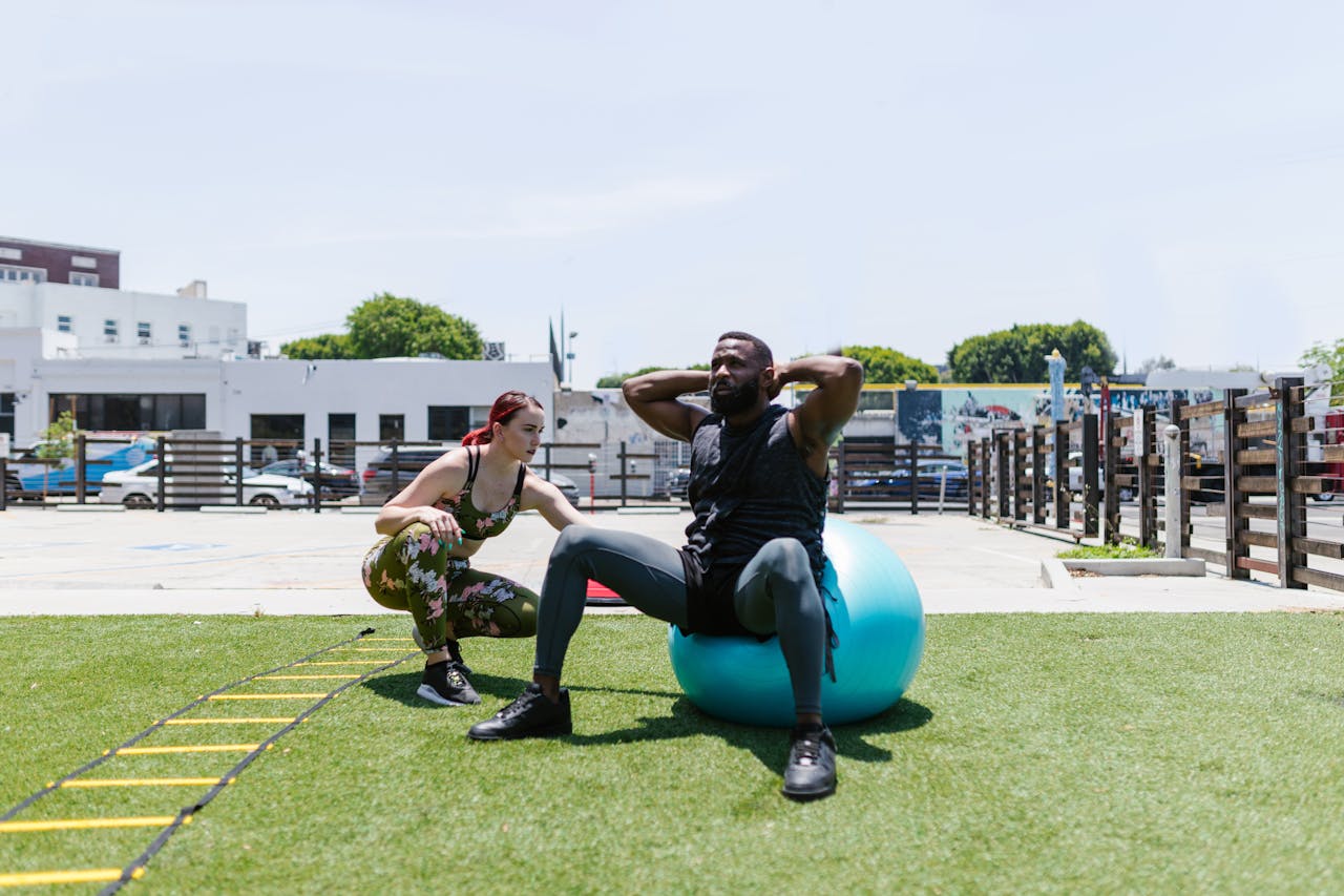Man and woman engaged in fitness activities outdoors using an exercise ball.